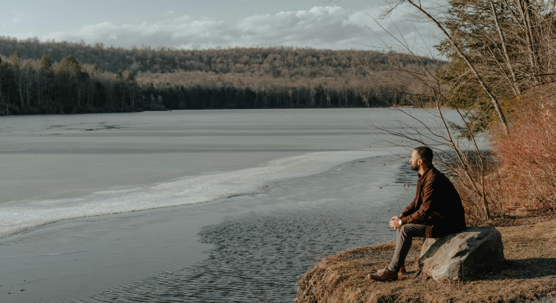 man sitting on a rock on the bank of a river